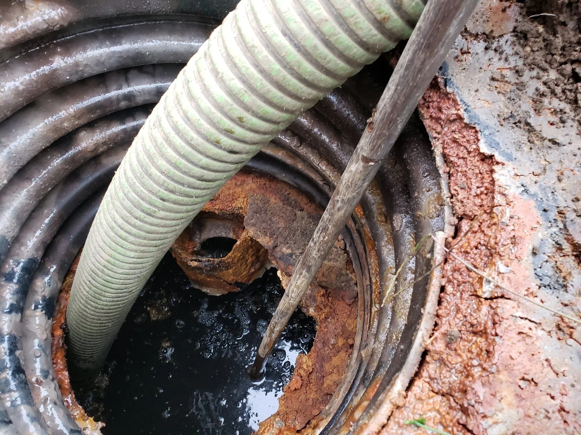 Vacuum hose and snake clearing a commercial septic tank port